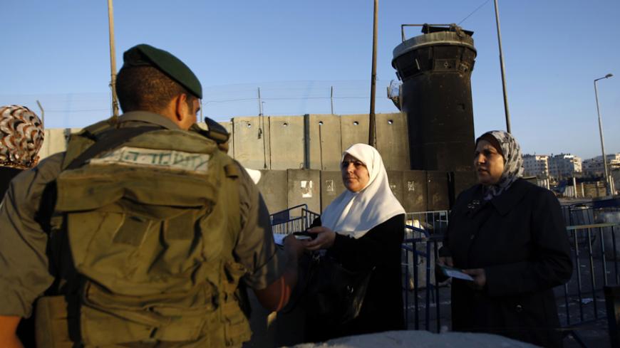 Palestinian women present their identity cards to an Israeli border police officer as they wait to make their way to Jerusalem to attend the first Friday prayer of Ramadan in al-Aqsa mosque, at Qalandia checkpoint near the West Bank city of Ramallah July 4, 2014. REUTERS/Mohamad Torokman (WEST BANK - Tags: POLITICS SOCIETY) - RTR3X1SO