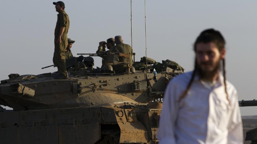 An ultra-Orthodox Jewish man walks near Israeli army tanks near the border with Gaza July 30, 2014. Israeli fire killed at least 43 Palestinians in the Gaza Strip early on Wednesday as the Jewish state said it targeted Islamist militants at dozens of sites across the coastal enclave, while Egyptian mediators prepared a revised ceasefire proposal. REUTERS/Siegfried Modola (ISRAEL - Tags: CIVIL UNREST MILITARY CONFLICT RELIGION POLITICS) - RTR40LLQ