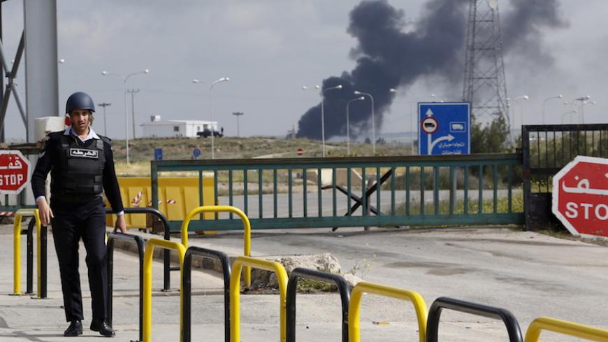 A member of Jordanian security walks near the main Jaber border crossing in the Jordanian city of Mafraq, April 2, 2015, as smoke rises on the Syrian side after violence broke out near the border. Jordan said it had temporarily closed its border crossing with Syria on Wednesday because of violence on the other side of the frontier, a move it described as a precautionary measure. Mainstream Syrian rebels seized the Nasib border crossing with Jordan from the Syrian government on Wednesday, the leader of one o
