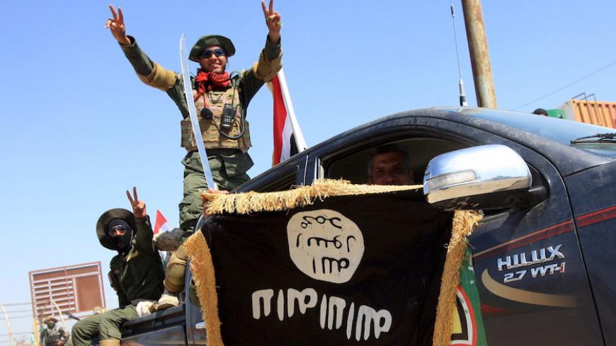 Shi'ite paramilitary fighters hold an Islamist State flag which they pulled down during victory celebrations after returning from Tikrit in Kerbala, southwest of Baghdad April 4, 2015.  Shi'ite paramilitaries started leaving Tikrit on Saturday following a government deal after locals complained that some fighters had spent several days looting the Sunni city after helping retake it from Islamic State.  REUTERS/Mushtaq Muhammed  - RTR4W3WJ