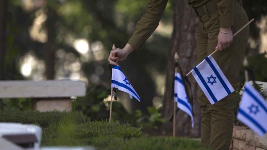 An Israeli soldier places flags on graves of fallen soldiers during a ceremony at the Mount Herzl military cemetery in Jerusalem, ahead of Memorial Day April 19, 2015. Israel commemorates its fallen soldiers on Memorial Day, which begins Tuesday night. REUTERS/Ronen Zvulun - RTR4XX69