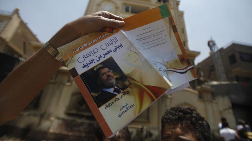 A protester, opposing Egyptian President Mohamed Mursi, holds a book titled "President Mursi Building a New Egypt" in front of the headquarters of the Muslim Brotherhood in Cairo's Moqattam district July 1, 2013. The Brotherhood said on Monday that armed men who ransacked its national headquarters had crossed a red line of violence, and the movement was considering action to defend itself. Hundreds of people threw petrol bombs and rocks at the building, which caught fire as guards and Brotherhood members in