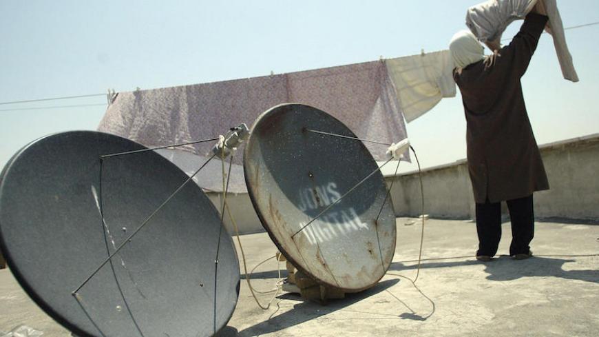 TO GO WITH AFP STORY IRAN-POLITICS-SATELLITE-JAMMING: An Iranian woman, standing next to two satellite dishes, hangs washed laundry on the roof of her house in Tehran, 12 June 2003. Owning satellite equipment and viewing uncensored international channels is strictly banned in the Islamic republic. Yet many people purchase satellite dishes and receivers illegally and enjoy watching Persian-language TV broadcasts from overseas, among other channels. However, according to the local press, Iranian authorities h