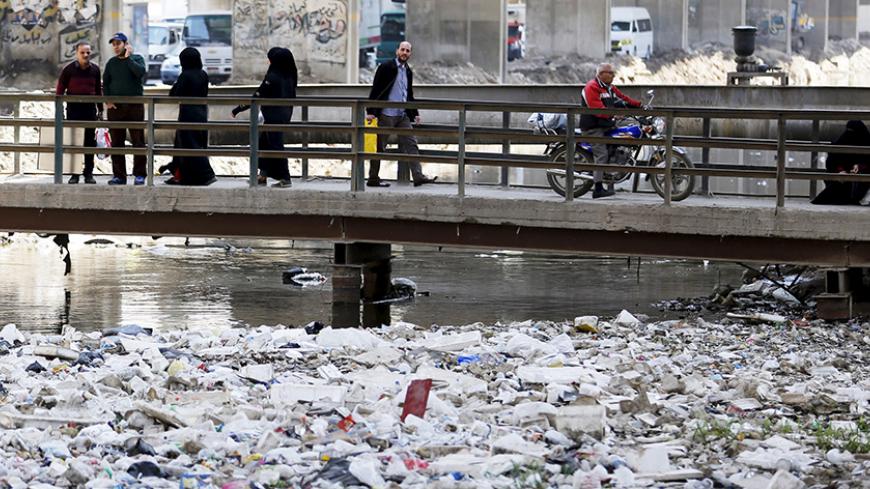 People walk across a bridge surrounded by litter and waste at a canal connected to the river Nile in Cairo March 22, 2015.  World Water Day is observed on March 22.  REUTERS/Amr Abdallah Dalsh - RTR4UD5Y