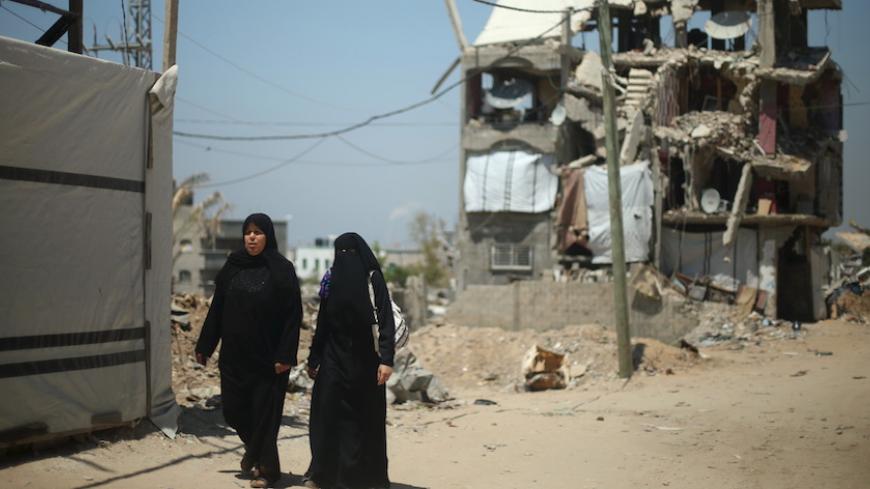 Palestinian women walk in front of a house that witnesses said was destroyed by Israeli shelling during a 50-day war last summer, in the east of Gaza City May 6, 2015. In recent weeks, a flurry of envoys has beaten a path to Gaza's door: representatives from Qatar, Turkey, the United Nations, the European Union and former U.S. president Jimmy Carter have all visited or tried to visit. The impact of the stand-off is widespread, but in two areas it is particularly problematic: it is stalling rebuilding in Gaz