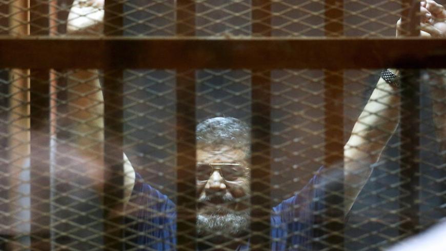 Former Egyptian President Mohamed Mursi waves during his trial at a court in the outskirts of Cairo, May 16, 2015. An Egyptian court on Saturday sought the death penalty for former president Mohamed Mursi and more than 100 other members of the Muslim Brotherhood in connection with a mass jail break in 2011. REUTERS/Mohamed Abd El Ghany - RTX1D7JE