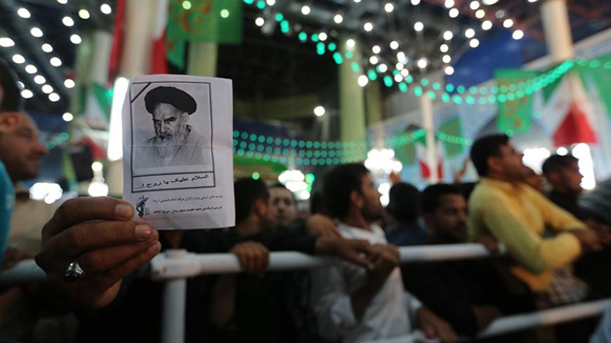 An Iranian man holds a photo of late Ayatollah Ruhollah Khomeini, while listening to Iran's President Hassan Rouhani delivering a speech on the eve of the 25th anniversary of the death of Islamic revolutionary leader Khomeini, at Khomeini's mausoleum in a suburb of Tehran on June 3, 2014. AFP PHOTO / ATTA KENARE        (Photo credit should read ATTA KENARE/AFP/Getty Images)