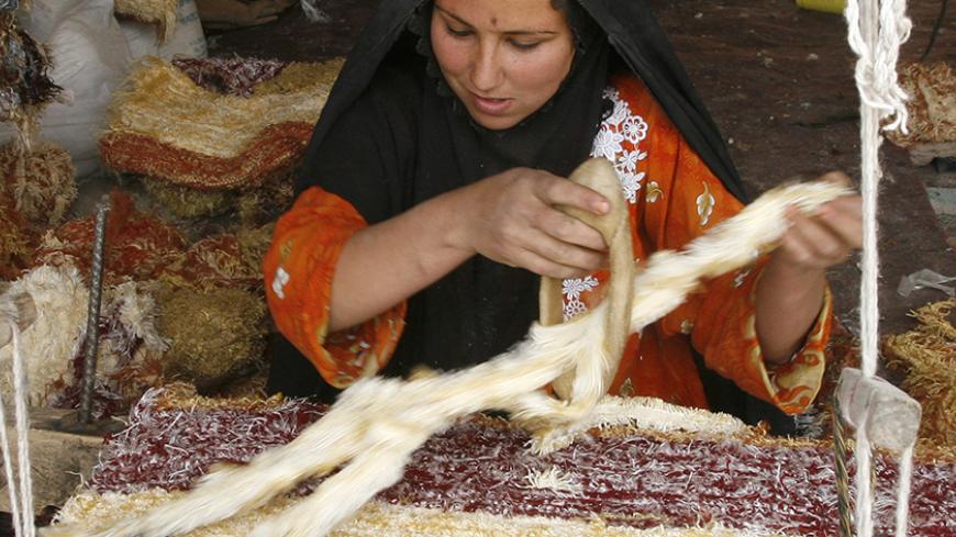 A woman uses a traditional knitting machine to make a carpet in Baghdad's Sadr city, April 3, 2007.    REUTERS/Kareem Raheem       (IRAQ) - RTR1O9DA