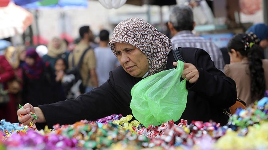 A Palestinian woman buys candies from a vendor at a market ahead of Eid al-Adha in the West Bank city of Nablus September 30, 2014. REUTERS/Abed Omar Qusini (WEST BANK  - Tags: RELIGION SOCIETY) - RTR48DQO