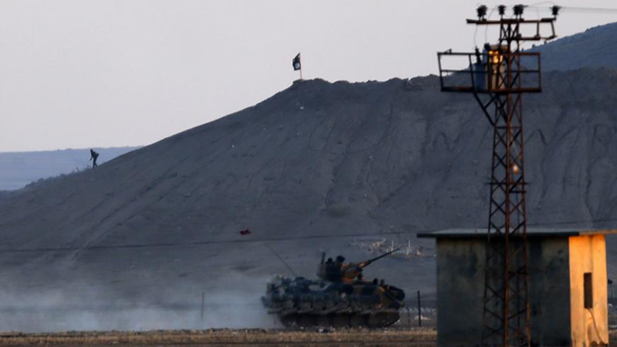 An Islamic State fighter walks near a black flag belonging to the Islamic State as a Turkish army vehicle takes position near the Syrian town of Kobani, as pictured from the Turkish-Syrian border near the southeastern town of Suruc, Sanliurfa province October 7, 2014. Turkey has asked the United States to step up air strikes to keep Islamic State militants from seizing a key Syrian Kurdish border town, a senior Turkish official was quoted as saying on Tuesday. Islamic State fighters advancing into the south