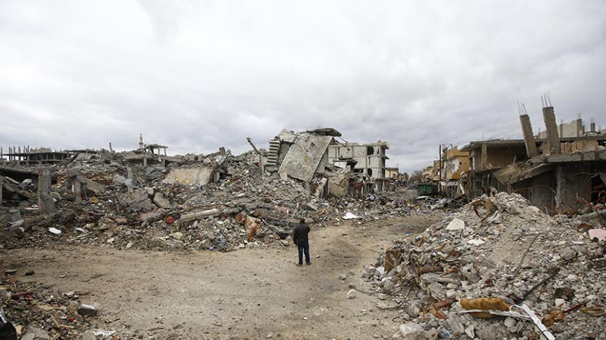 A man walks past abandoned buildings in the northern Syrian town of Kobani January 30, 2015. Sheets meant to hide residents from snipers' sights still hang over streets in the Syrian border town of Kobani, and its shattered buildings and cratered roads suggest those who fled are unlikely to return soon. Kurdish forces said this week they had taken full control of Kobani, a mainly Kurdish town near the Turkish border, after months of bombardment by Islamic State, an al Qaeda offshoot that has spread across S