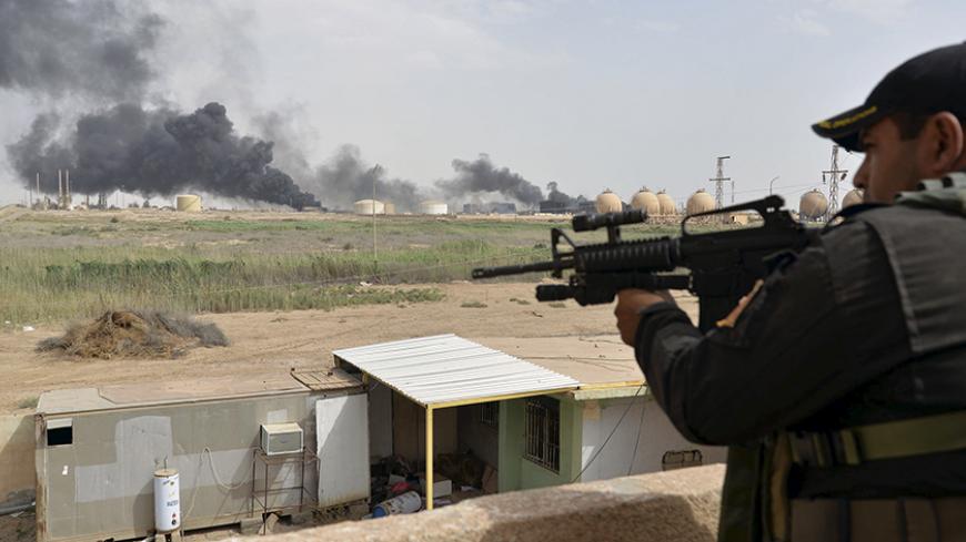 A member from the Iraqi security forces guards as smoke rises from Baiji oil refinery, north of Baghdad, Iraq May 26, 2015. Iraq's Shi'ite paramilitaries said on Tuesday they had taken charge of the campaign to drive Islamic State from the western province of Anbar, giving the operation an openly sectarian codename that could infuriate its Sunni Muslim population. Picture taken May 26, 2015.  REUTERS/Stringer - RTX1EOY1
