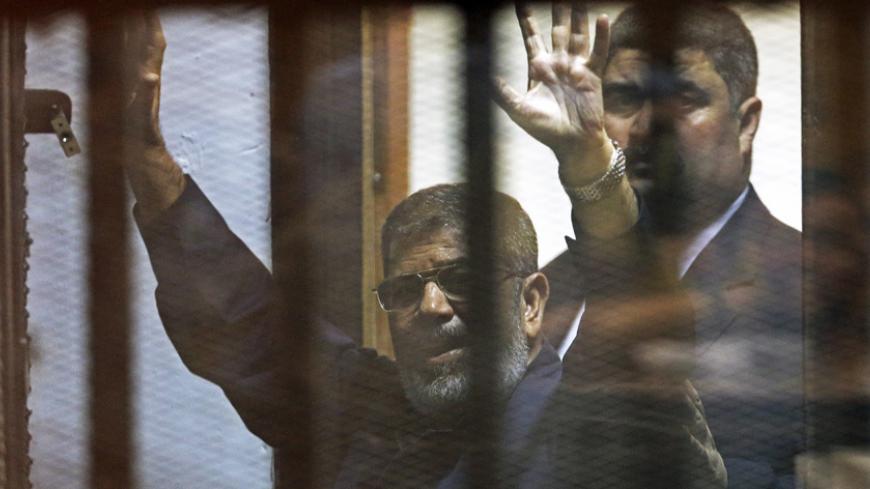 Deposed Egyptian President Mohamed Mursi greets his lawyers and people from behind bars after his verdict at a court on the outskirts of Cairo, Egypt June 16, 2015. An Egyptian court sentenced deposed President Mohamed Mursi to death on Tuesday on charges of killing, kidnapping and other offences during a 2011 mass jail break.The general guide of the Muslim Brotherhood, Mohamed Badie, and four other Brotherhood leaders were also handed the death penalty. More than 80 others were sentenced to death in absent