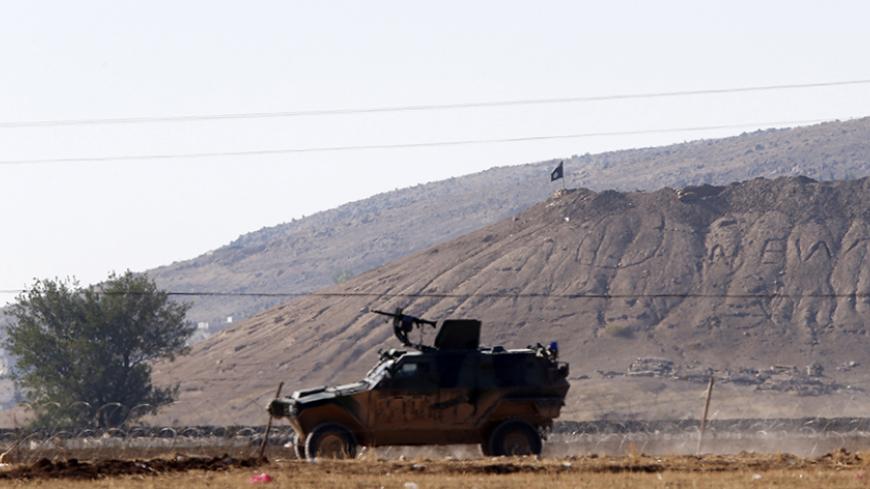 A black flag belonging to Islamic State is seen near the Syrian town of Kobani as a Turkish army vehicle takes up position on the Turkish-Syrian border near the southeastern town of Suruc in Sanliurfa province October 7, 2014. Islamic State fighters advanced into the south west of the Syrian Kurdish town of Kobani overnight, a monitoring group said on Tuesday, taking several buildings to gain attacking positions from two sides of the city.  REUTERS/Umit Bektas (TURKEY - Tags: CIVIL UNREST MILITARY CONFLICT 