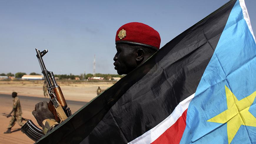 An SPLA soldier is pictured behind a South Sudan flag as he sits on the back of a pick-up truck in Bentiu, Unity state January 12, 2014. South Sudan's army said on Friday it had regained the rebel-held town of Bentiu, restoring government control of Unity state where oil production had been halted by fighting. The rebels said they made a "tactical withdrawal" from Bentiu to avoid civilian casualties.  REUTERS/Andreea Campeanu (SOUTH SUDAN - Tags: CIVIL UNREST POLITICS CONFLICT) - RTX17AO2
