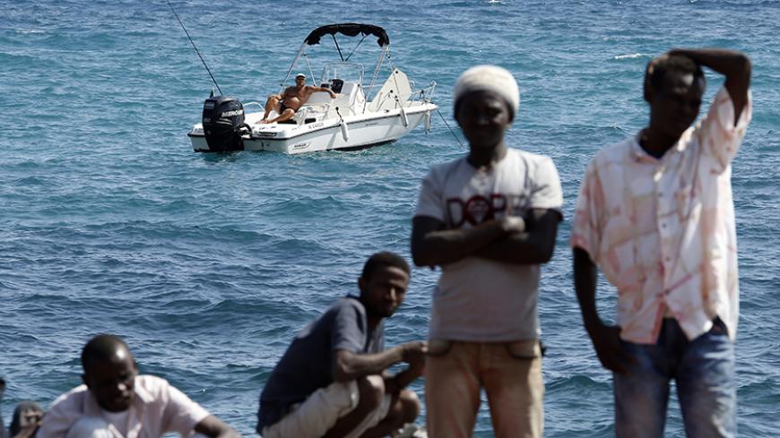 A man fishes from his boat as a group of migrants gather on the seawall at the Saint Ludovic border crossing on the Mediterranean Sea between Vintimille, Italy and Menton, France, June 14, 2015. On Saturday, some 200 migrants, principally from Eritrea and Sudan who attempted to cross the border, were blocked by Italian police and French gendarmes.   REUTERS/Eric Gaillard  TPX IMAGES OF THE DAY - RTX1GFZS