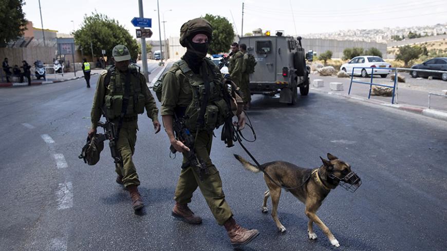 Israeli soldiers walk with a dog next to an Israeli checkpoint near the West Bank town of Bethlehem, after a stabbing attack June 29, 2015. A statement from the Israeli police said on Monday a Palestinian woman stabbed an Israeli border policewoman at the crossing between Bethlehem and Jerusalem. REUTERS/Ronen Zvulun  - RTX1I8C3