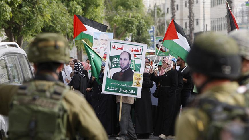 Israeli soldiers stand guard as Palestinians hold national flags and  posters of jailed relatives during a protest in solidarity with prisoners on hunger strike,in the West Bank city of Hebron June 4, 2014. Some 120 Palestinians jailed without trial in Israel have been on an open-ended hunger strike, eating only salt and drinking water, since April 24 to demand an end to so-called "administrative detention". REUTERS/Mussa Qawasma (WEST BANK - Tags: POLITICS CIVIL UNREST) - RTR3S7JN