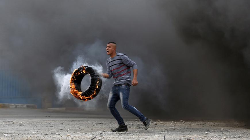 A Palestinian protester moves a burning tyre during clashes with Israeli troops at a protest against Jewish settlements, in Jalazoun refugee camp near the West Bank city of Ramallah March 27, 2015.   REUTERS/Mohamad Torokman       TPX IMAGES OF THE DAY      - RTR4V667