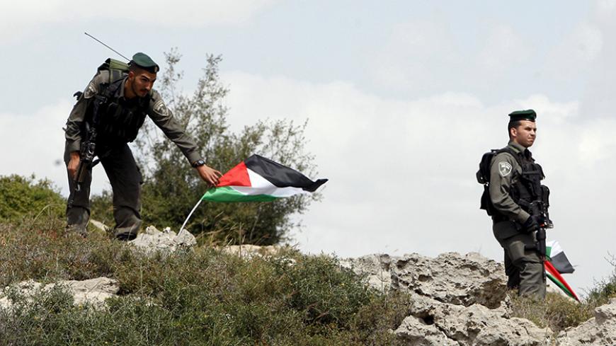Israeli border policeman remove Palestinian flags during a demonstration by Palestinians marking Land Day and against Jewish settlements in Wadi Foukeen near the West Bank city of Bethlehem March 30, 2015. Palestinians mark Land Day on March 30, the annual commemoration of protests in 1976 against Israel's appropriation of Arab-owned land in the Galilee.  REUTERS/Mussa Qawasma - RTR4VGRL