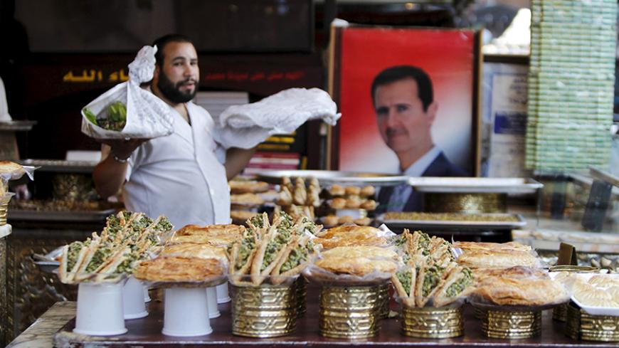 A vendor sells traditional sweets near a picture of Syria's President Bashar al-Assad during the Muslim fasting month of Ramadan in Damascus, Syria July 8, 2015. Picture taken July 8, 2015. REUTERS/Omar Sanadiki - RTX1JOL3