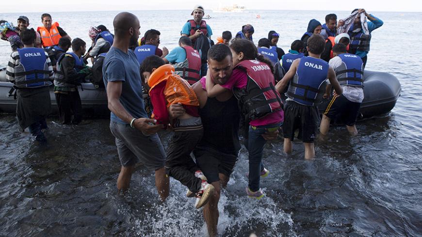 A Syrian refugee carries two children moments after arriving on a dinghy  on the Greek island of Lesbos, September 8, 2015. Greece asked the European Union for aid to prevent it being overwhelmed by refugees, as a minister said arrivals on Lesbos had swollen to three times as many as the island could handle.  REUTERS/Dimitris Michalakis - RTX1RPL9