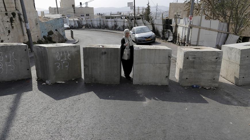 A woman passes through concrete blocks that were placed by Israeli police last week, in the East Jerusalem neighbourhood of Jabel Mukaber October 19, 2015. REUTERS/Ammar Awad   - RTS52BK