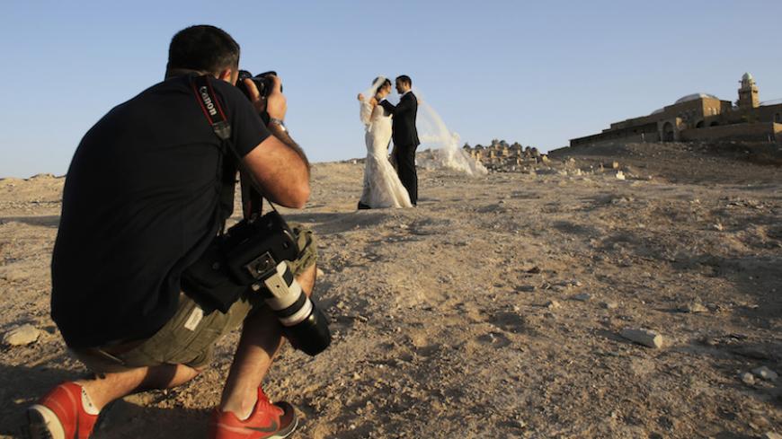 An Israeli couple poses for their wedding photographer as graves and a mosque (R) are seen in the background at Nabi Musa in the Judean desert near the West Bank city of Jericho November 28, 2013. REUTERS/Ammar Awad (WEST BANK - Tags: SOCIETY ENTERTAINMENT) - RTX15WK5