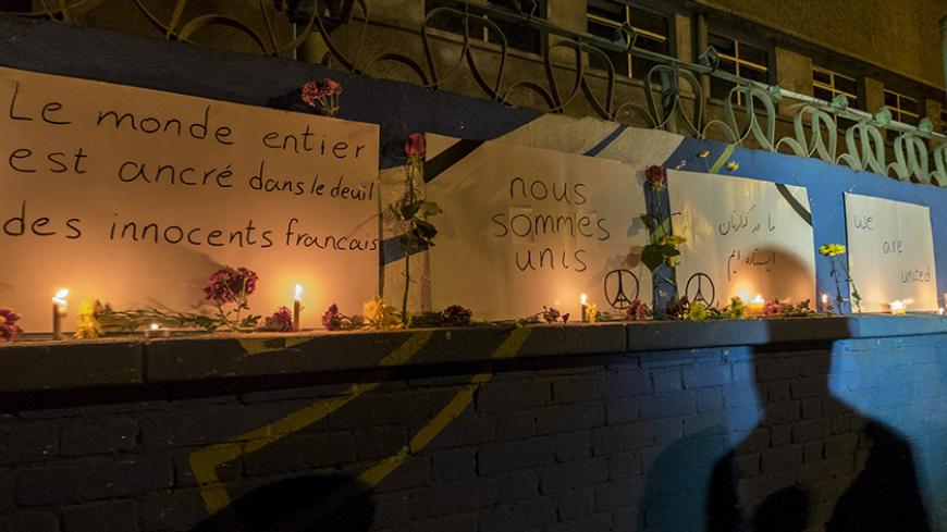 A shadow is cast on a wall as flowers and candles are seen in front of placards in tribute to the victims of Paris attacks, outside French embassy in Tehran, Iran November 14, 2015. REUTERS/Raheb Homavandi/TIMA ATTENTION EDITORS - THIS IMAGE WAS PROVIDED BY A THIRD PARTY. FOR EDITORIAL USE ONLY. - RTS71X3