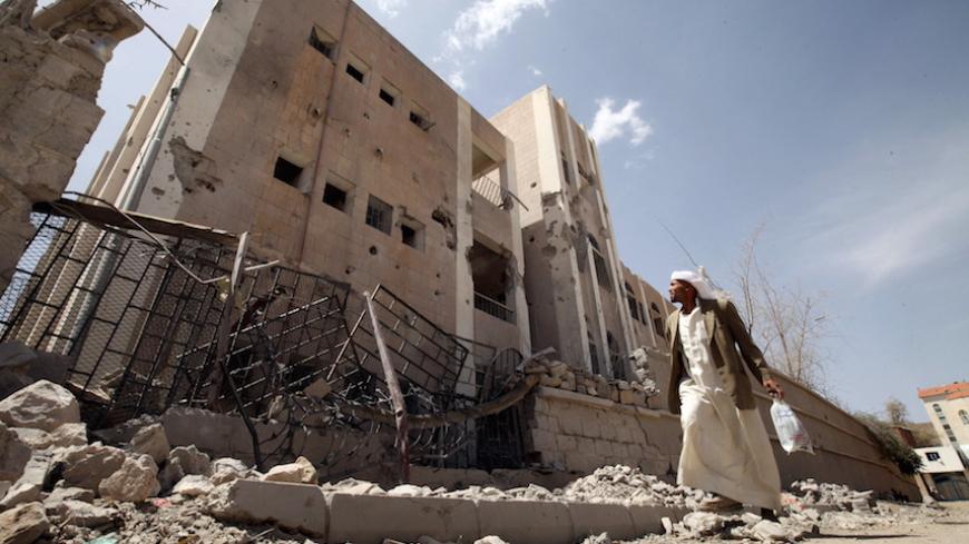 A man looks at a school destroyed by an air strike as he flees his home in Sanaa April 28, 2015. REUTERS/Mohamed al-Sayaghi - RTX1AO4I