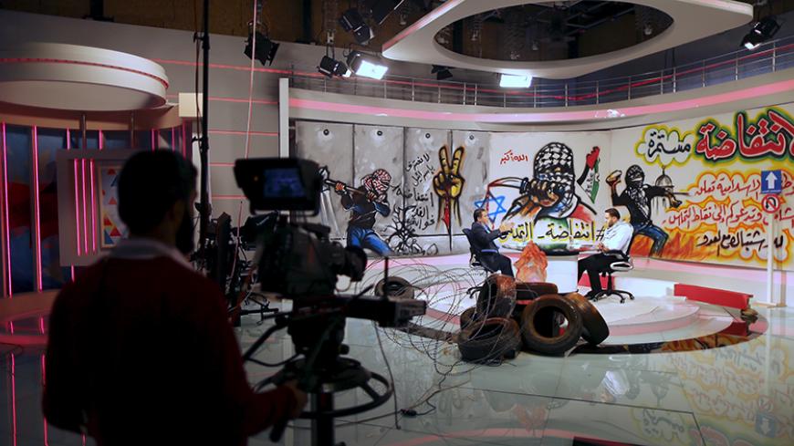 Palestinian presenter Raji Al-Hams (R) listens to Hamas official Salah al-Bardweel at the studio of Hamas-run Al-Aqsa TV in Gaza City October 27, 2015. The studio of Hamas-run Al-Aqsa TV is decorated with slogans praising the "knife intifada" against Israel. Video clips and rousing songs glorify the daily attacks, while the presenters all wear black-and-white Keffiyeh scarves. REUTERS/Mohammed Salem  - RTX1TG21