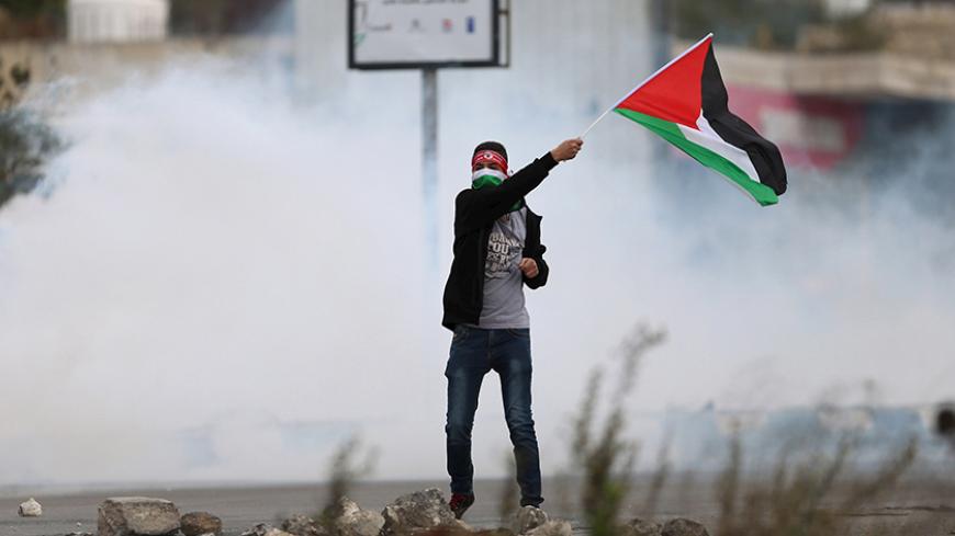 A protester waves a Palestinian flag in front of tear gas fired by Israeli troops during clashes at Hawara checkpoint near the West Bank city of Nablus November 28, 2015.  REUTERS/Ahmad Talat  - RTX1W883