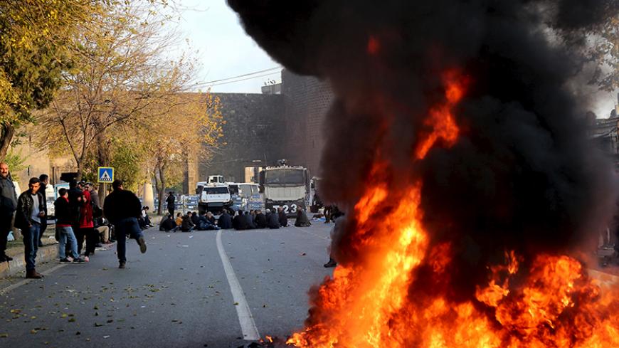 Demonstrators sit between a fire and police barricades during a protest against the curfew in Sur district in the Kurdish dominated southeastern city of Diyarbakir, Turkey, December 10, 2015. Seven Kurdish militants and a policeman have been killed in four days of fighting in a southeastern Turkish province that has been under curfew all week, security sources said. Nusaybin, a district of Turkey's southeastern province of Mardin on the Syrian border, has been under curfew since Sunday. Eight policemen were