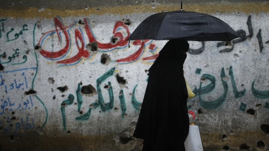 A Palestinian woman holds an umbrella to cover herself from rain as she makes her way to fill containers with water in Shejaia neighborhood, that witnesses said was devastated during a seven-week Israeli offensive, in the east of Gaza City October 19, 2014.  An open-ended ceasefire between Israel and Hamas-led Gaza militants, mediated by Egypt, took effect on August 26 after a seven-week conflict. It called for an indefinite halt to hostilities, the immediate opening of Gaza's blockaded crossings with Israe