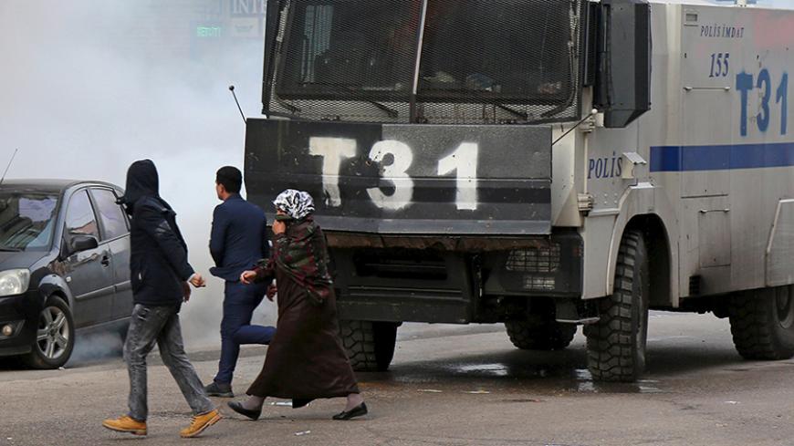 People walk past an armored police vehicle as Turkish riot police use tear gas to disperse Kurdish demonstrators during a protest against a curfew in Sur district and security operations in the region, in the southeastern city of Diyarbakir, Turkey January 17, 2016. REUTERS/Sertac Kayar - RTX22QXH