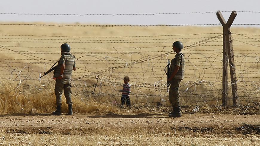 Turkish soldiers stand guard as a Syrian refugee boy waits behind the border fences to cross into Turkey on the Turkish-Syrian border, near the southeastern town of Akcakale in Sanliurfa province, Turkey, June 5, 2015. More than 3,000 Syrians fleeing clashes between Islamic State and Kurdish fighters have crossed into Turkey since Wednesday, a Turkish government official said. Kurdish forces are trying to drive the militants out of Tel Abyad, in Syria's Hassakah province, close to the Turkish border town of