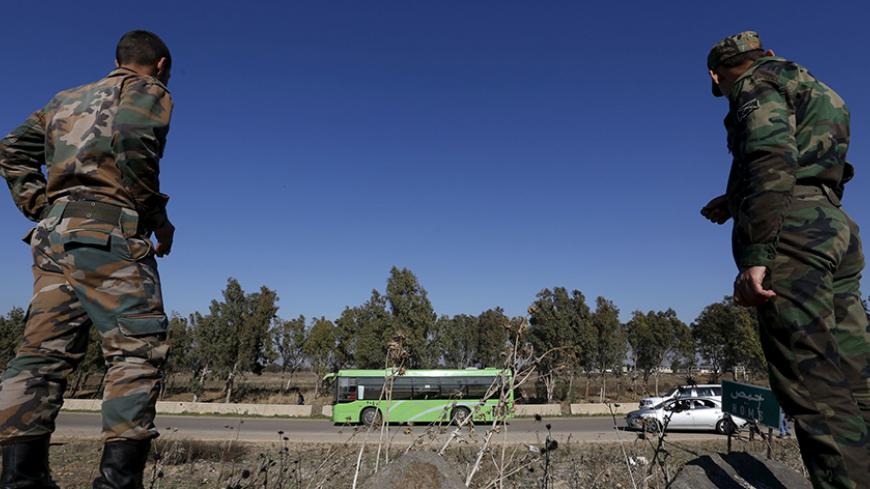 Syrian Army forces look on as buses leave district of Waer during a truce between the government and rebels, in Homs, Syria December 9, 2015. Scores of people left the last area held by insurgents in the Syrian city of Homs on Wednesday under a local truce between the government and rebels, a monitoring group said, a rare agreement in Syria's nearly five-year conflict. Three buses carrying people had left the previously besieged district of Waer, the Syrian Observatory for Human Rights said. About 750 peopl