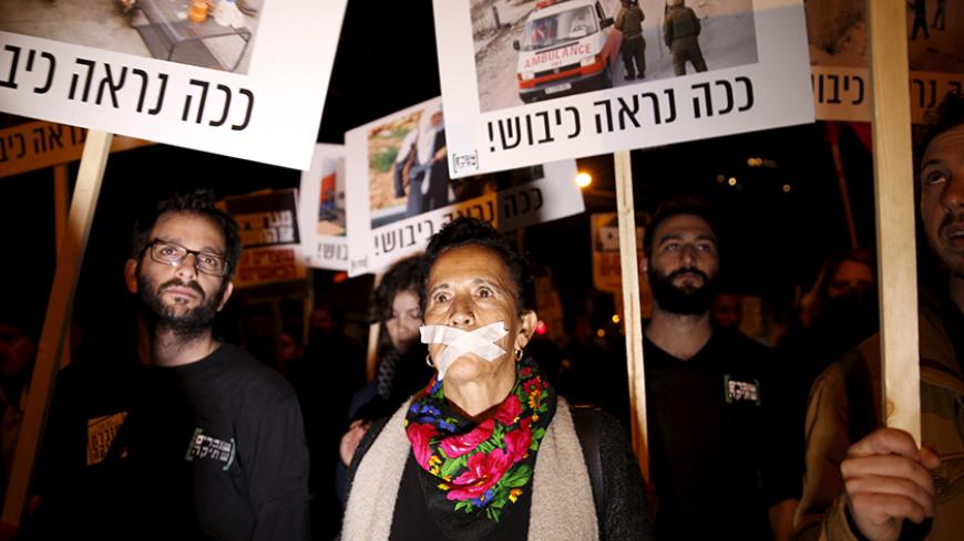 Israeli left wing demonstrators march holding placards protesting the right wing incitement against President Reuven Rivlin and human rights activists in Tel Aviv. December 19, 2015. An ultra-nationalist Israeli group has published a video accusing the heads of four of Israel's leading human rights organisations of being foreign agents funded by Europe and supporting Palestinians "involved in terrorism". The sign reads, "That's how occupation looks like." REUTERS/Baz Ratner - RTX1ZETR