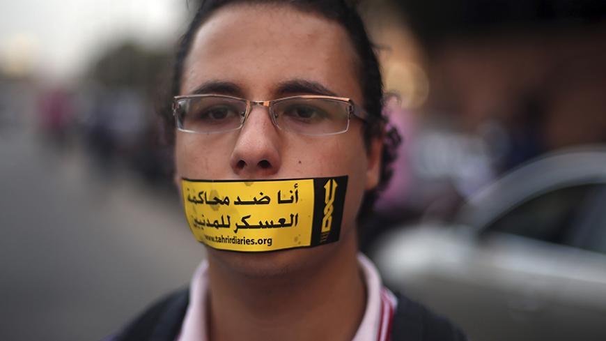 A demonstrator looks on with a sign reading "I am against the military courts for civilians" taped over his mouth during a human chain by members of the April 6 movement and liberal activists against a law restricting demonstrations as well as the crackdown on activists and calling for the release of activists in detention in front of El-Thadiya Egyptian Presidential in Cairo, April 23, 2014. REUTERS/Amr Abdallah Dalsh (EGYPT - Tags: POLITICS CIVIL UNREST) - RTR3MD2M