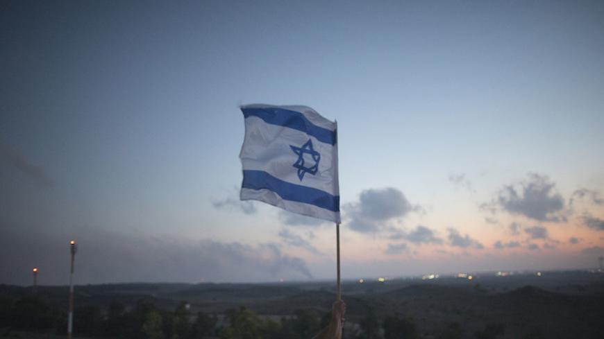 An Israeli man holds up a flag atop a hill overlooking the Gaza Strip in the southern town of Sderot July 20, 2014. More than 60 Palestinians and 13 Israeli soldiers were killed as Israel shelled a Gaza neighbourhood and battled militants on Sunday in the bloodiest fighting in a near two-week-old offensive. REUTERS/Ronen Zvulun (ISRAEL - Tags: CONFLICT CIVIL UNREST POLITICS) - RTR3ZFUS