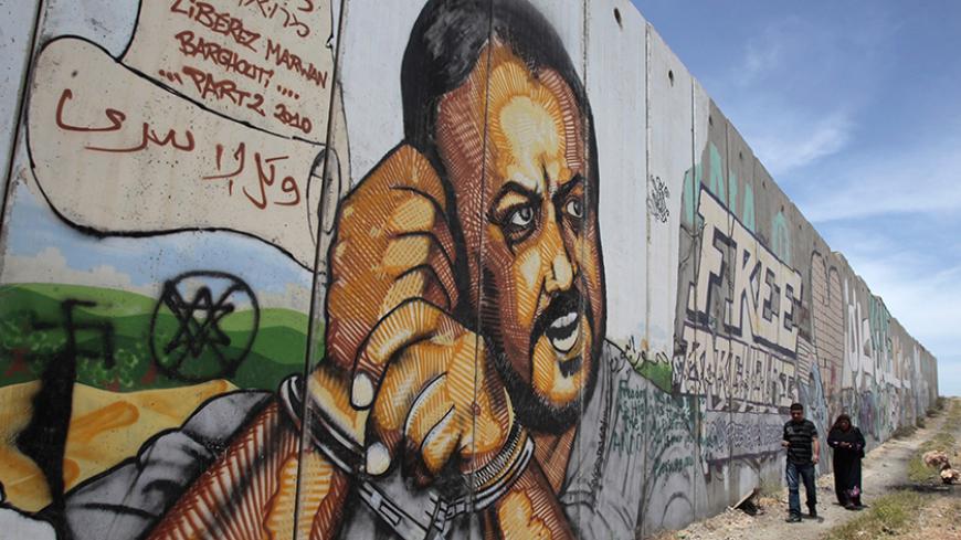 Palestinians walk past graffiti depicting jailed Fatah leader Marwan Barghouti on a section of the controversial Israeli barrier near the Qalandiya checkpoint outside the West Bank city of Ramallah May 25, 2011. Palestinians and Israelis alike saw little prospect of a fresh start to Middle East peace talks on Wednesday after Israeli Prime Minister Benjamin Netanyahu's keynote speech to Congress. REUTERS/Baz Ratner (WEST BANK - Tags: POLITICS) - RTR2MVS6