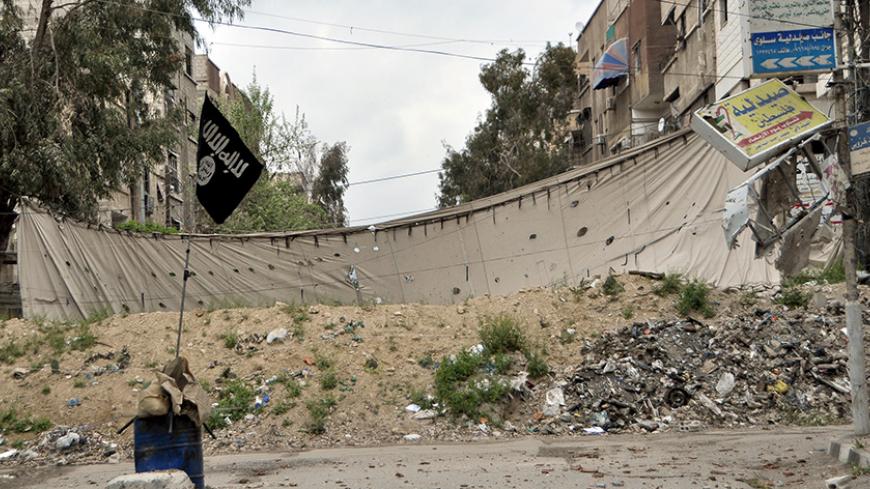 An Islamic State flag is seen near a barricade, which serves as protection from snipers of forces loyal to Syria's President Bashar al-Assad, in Yarmouk Street, the main street of Yarmouk camp, April 10, 2015. A bout of fighting between militants over control of the Yarmouk refugee camp on the edge of Damascus has only compounded the misery of residents already suffering from acute shortages of food, clean water and power. Picture taken April 10, 2015. REUTERS/Moayad Zaghmout - RTR4XFKQ