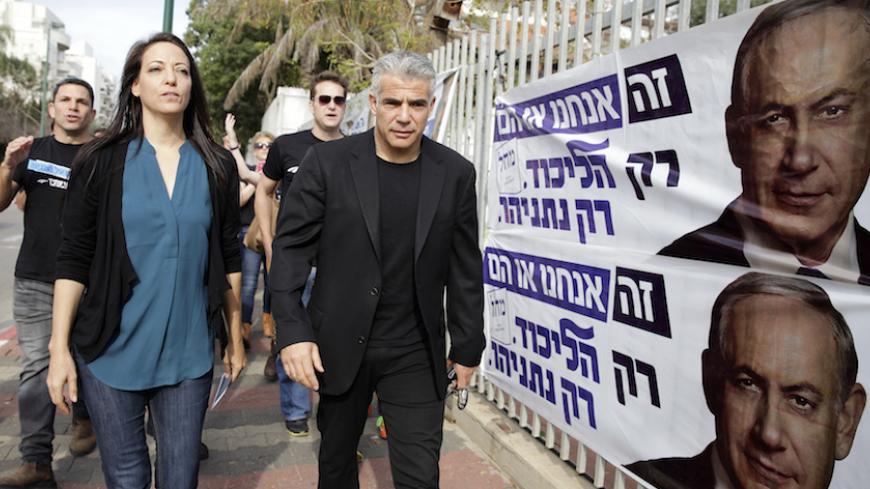 Yesh Atid leader Yair Lapid (R) and his wife Lihi walk past Likud election campaign posters depicting Israeli Prime Minister Benjamin Netanyahu as they walk to a polling station in Tel Aviv March 17, 2015. Netanyahu's march towards becoming the longest-serving leader of Israel could be halted on Tuesday in an election that has exposed public fatigue with his stress on national security rather than socio-economic problems. Once a heartthrob television news anchor, Lapid, 51, was the rising star of Israeli po