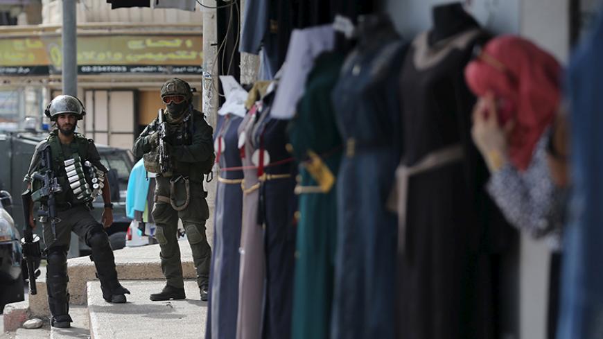 Israeli border policemen take position as a Palestinian woman looks out a shop during clashes in the West Bank town of Al-Ram, near Jerusalem October 22, 2015. Nine Israelis have been killed in Palestinian stabbings, shootings and vehicle attacks since the start of October. Forty-nine Palestinians, including 25 assailants, among them children, have been killed in attacks and during anti-Israeli protests. Among the causes of the turmoil is Palestinians' anger at what they see as Jewish encroachment on the al