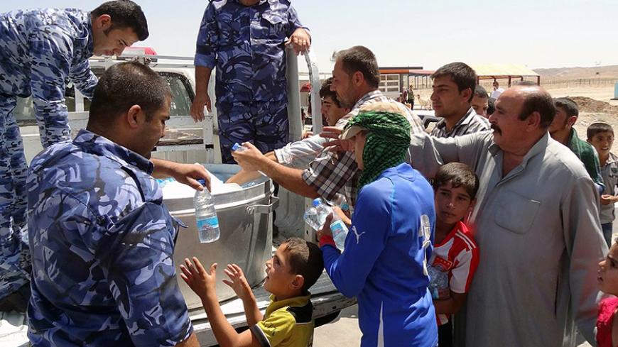Iraqi military personnel distribute water to Shiite Iraqi Kurds, known as "Shabak", displaced by fierce fighting between Kurdish peshmerga forces and jihadist militants from the Islamic State (IS) after arriving on the road between Kirkuk and Arbil having fled the area of Bartala near the northern Iraqi city of Mosul, on August 8, 2014. Jihadists seized Iraq's largest dam north of their hub of Mosul, giving them control over the supply of water and electricity for a vast area, officials said. AFP PHOTO / MA