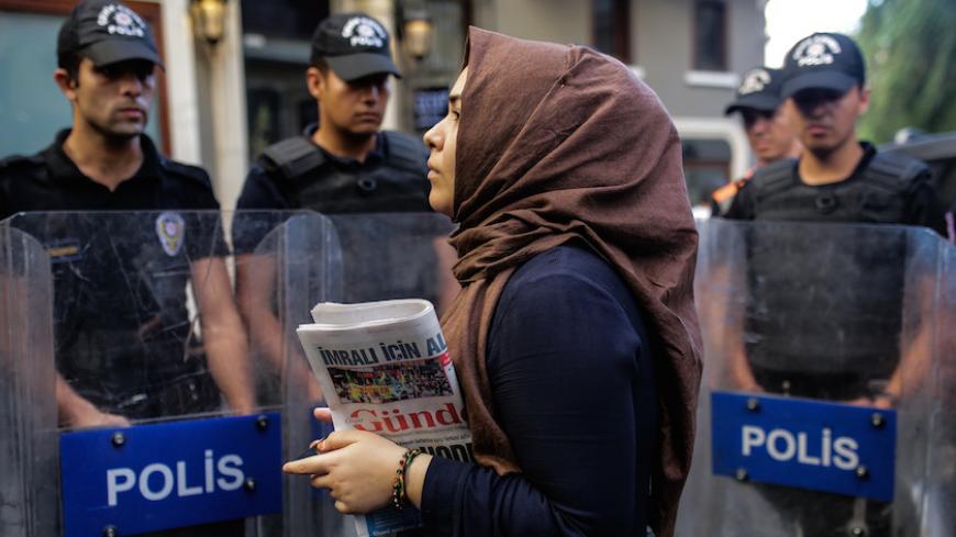 A woman holds a "Ozgur Gundem" newspaper in front of a police barricade on August 16, 2016 in Istanbul. 
A Turkish court has ordered the temporary closure of a newspaper accusing it of links with Kurdish militants and spreading terrorist propaganda. / AFP / YASIN AKGUL        (Photo credit should read YASIN AKGUL/AFP/Getty Images)