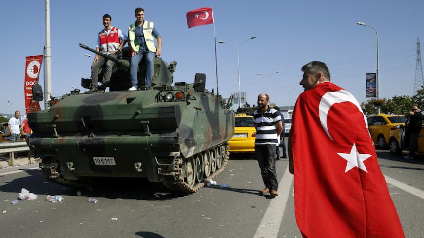 A man wrapped in a Turkish flag walks past a military vehicle in front of Sabiha Airport, in Istanbul, Turkey July 16, 2016. REUTERS/Baz Ratner - RTSI8VV