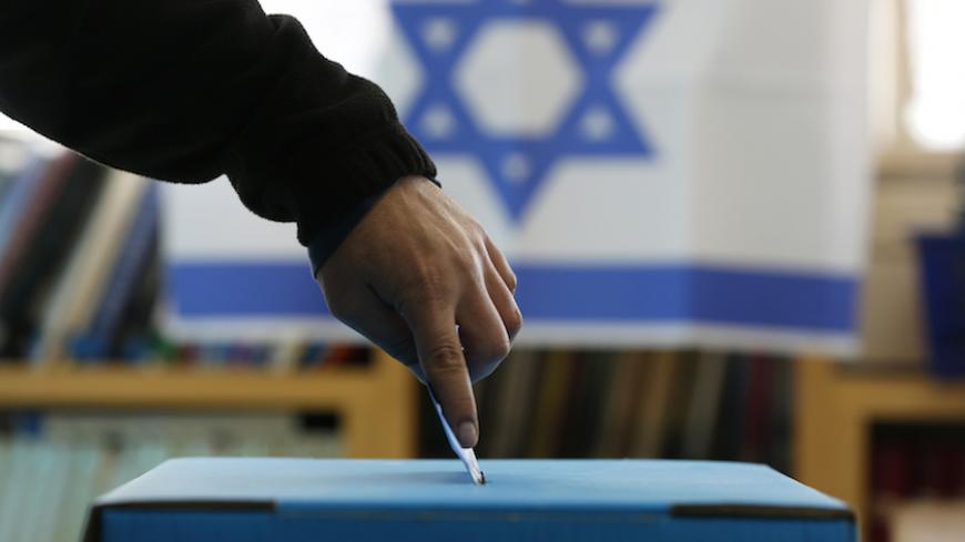 An Israeli flag is seen in the background as a man casts his ballot for the parliamentary election at a polling in the West Bank Jewish settlement of Ofra, north of Ramallah January 22, 2013. Israelis voted on Tuesday in an election that is expected to see Prime Minister Benjamin Netanyahu win a third term in office, pushing the Jewish state further to the right, away from peace with the Palestinians and towards a showdown with Iran. REUTERS/Baz Ratner (WEST BANK - Tags: POLITICS ELECTIONS TPX IMAGES OF THE