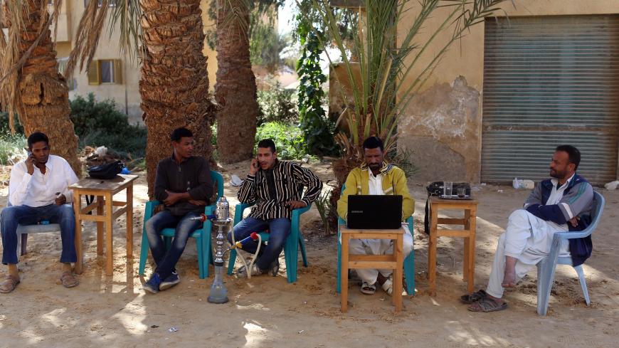 Men smoke and use their mobile phones as they sit at a small cafe in Siwa, November 22, 2014. Residents of Siwa have been hurt by declining tourism in Egypt, which received 9.5 million tourists last year, down from over 14.7 million tourists in 2010, before the uprising that ousted autocrat Hosni Mubarak. Nationwide, the situation is gradually improving and the government says tourism could recover to pre-crisis levels next year if regional turmoil spares Egypt. But Siwa, located just 50 km (30 miles) from 