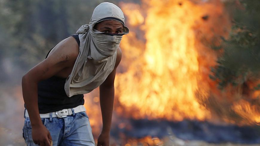 A Palestinian stone-thrower looks on as he stands in front of a fire during clashes with Israeli troops following the funeral of Palestinian Riham Dawabsheh at Duma village near the occupied West Bank city of Nablus, September 7, 2015. The mother of a Palestinian toddler killed in a July arson attack in the Israeli-occupied West Bank, died on Monday of her burns, the third fatality after her husband succumbed to his injuries last month. Suspected Jewish attackers torched the family's home in the northern We